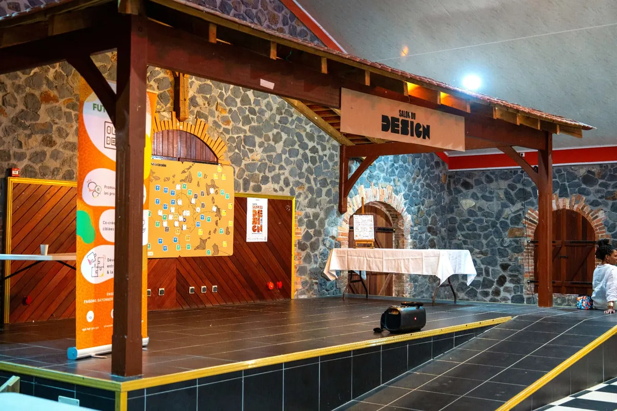 Scène du Salon du Design aménagée dans une salle en pierre, avec panneaux d'exposition et carte des îles de la Caraïbe