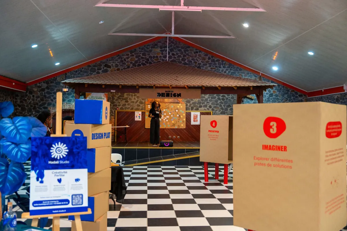 Scénographie du Salon du Design : parcours jalonné de stands en carton numérotés menant à une scène aménagée pour la prise de parole