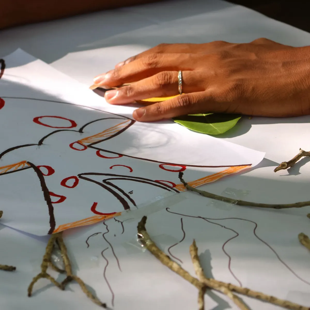 Main d'une participante martiniquaise posée sur un dessin réalisé avec des branchages pendant un atelier de design